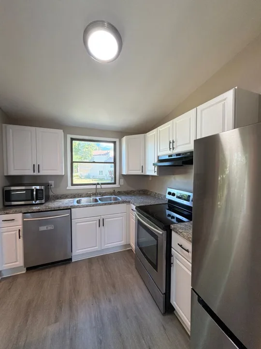 White cabinets, dark hardware, stainless-steel appliances, and wood-look flooring give this kitchen a bright, coordinated finish.