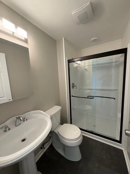 A black-framed glass shower enclosure, pedestal sink, and neutral walls make the most of this compact bathroom.