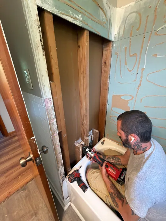 Wall sections beside the bathtub have been removed to expose the framing while renovation work is underway.