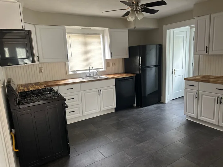 White cabinetry, wood-tone countertops, and black appliances create a balanced kitchen with contrasting dark flooring.