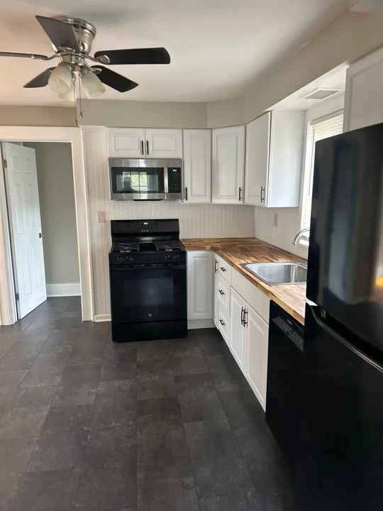 The cooking area pairs black appliances with white cabinets and wood-tone work surfaces, with a clear path through the kitchen.