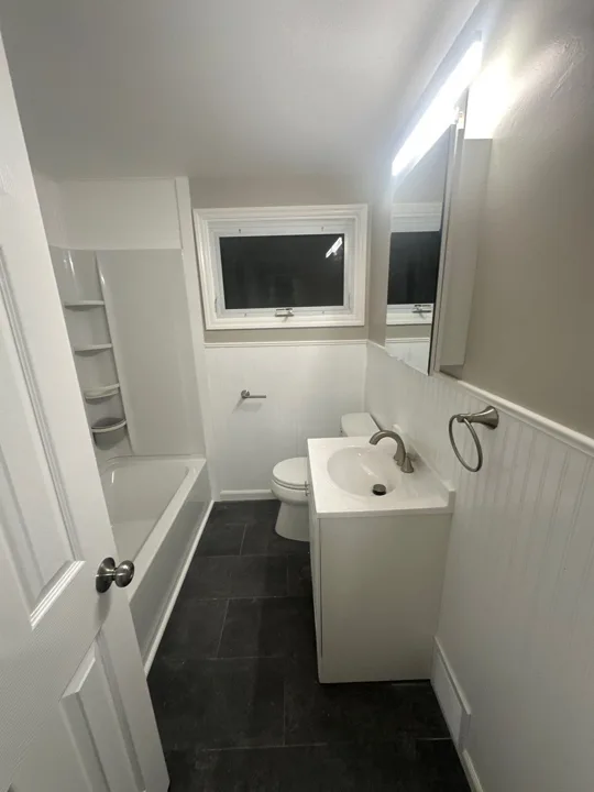 A white vanity, matching wall paneling, and dark flooring give this narrow bathroom a clean, cohesive appearance.