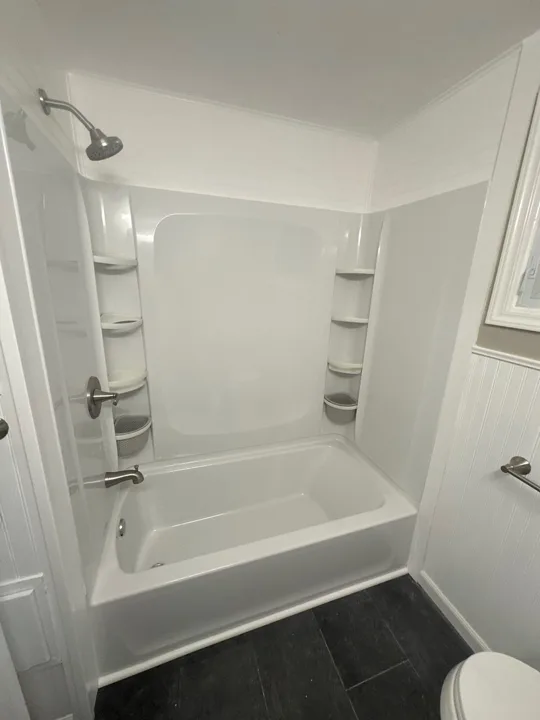 A white tub and shower surround with built-in shelves provides a simple, practical bathing space.