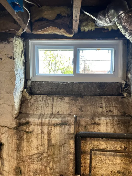 A white-framed window is fitted in the opening while the surrounding wall and ceiling remain exposed for finishing work.